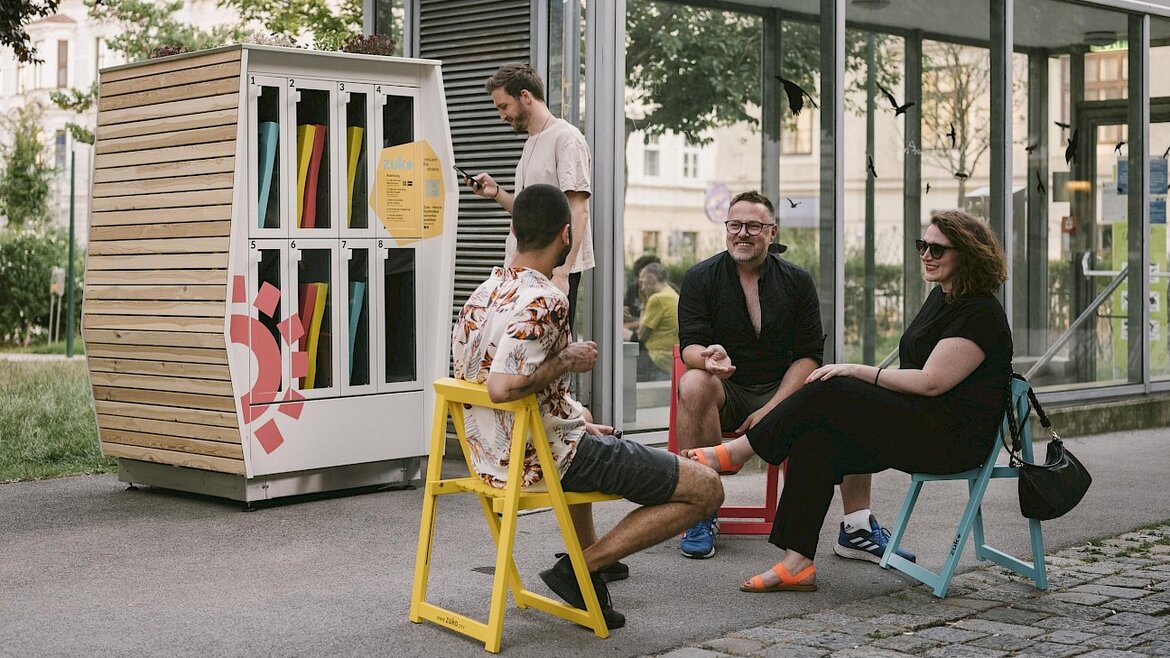Menschen sitzen auf bunten Klappstühlen in zentraler Lage einer Stadt