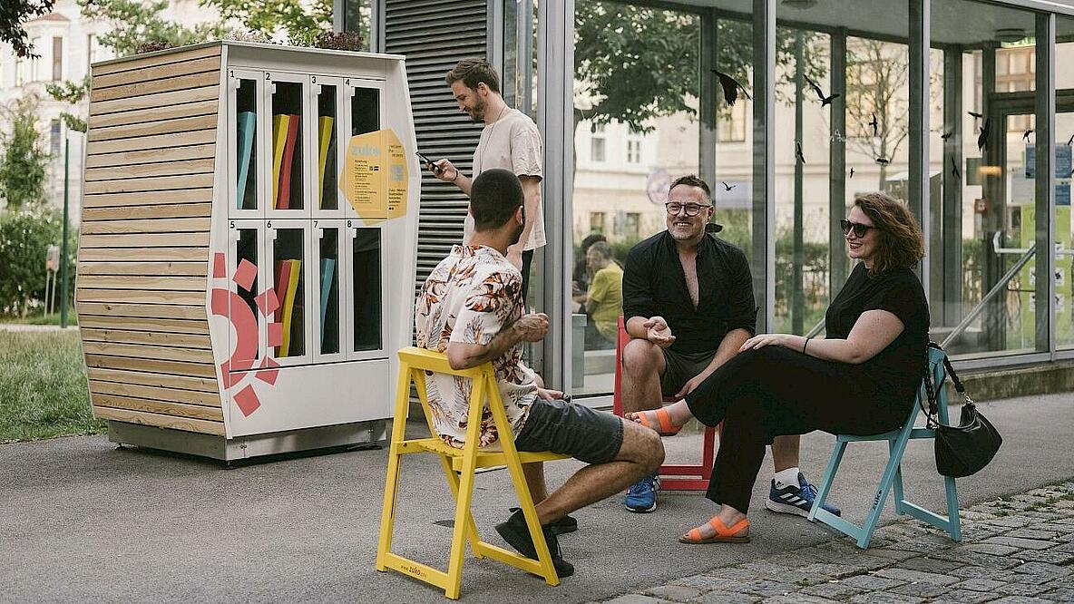 Menschen sitzen auf bunten Klappstühlen in zentraler Lage einer Stadt