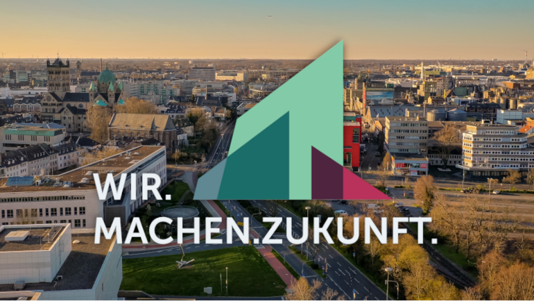 Überblick über die Stadt Neuss, darüber Motto der Mitgliederversammlung des Deutschen Städtetages "Wir.Machen.Zukunft"