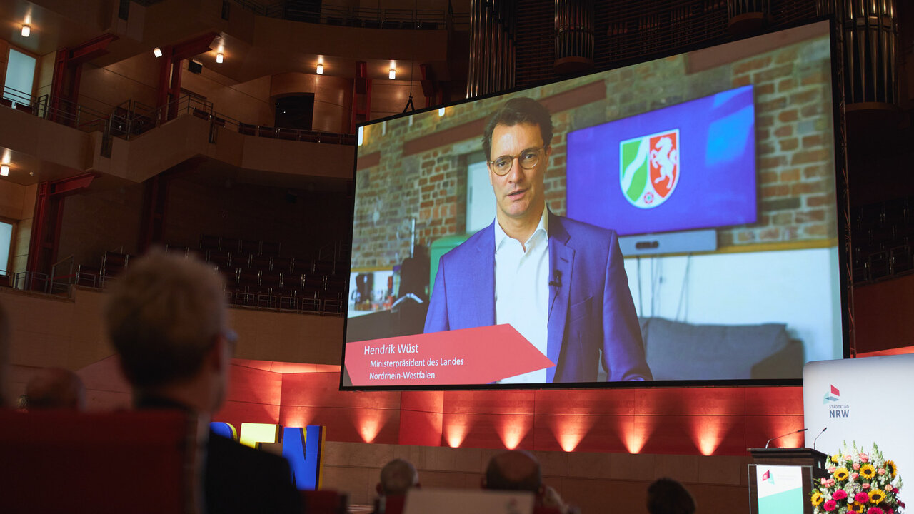 Die Delegierten der Mitgliederversammlung schauen auf das Video-Grußwort von Ministerpräsident Hendrik Wüst