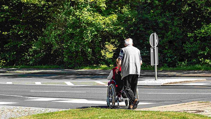 Mann schiebt Rollstuhl.