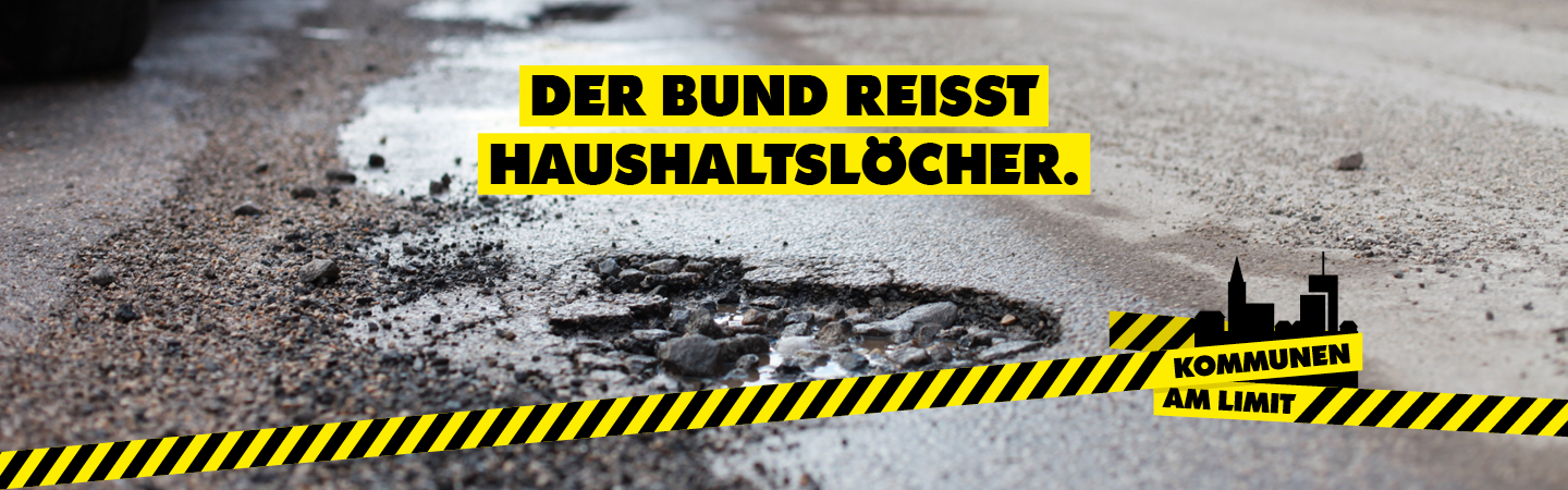 Kampagnenmotiv zum Aktionstag "Kommunen am Limit": Blick auf ein Schlagloch im Straßenbelag, darüber der Slogan "Der Bund reißt Haushaltslöcher"